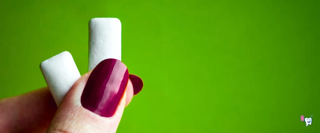 Two white chewing gums held in the fingers of a woman with dark red painted nails on a green background | Source: shutterstock | For article: Chewing Gum | For website: healthychewinggum.com