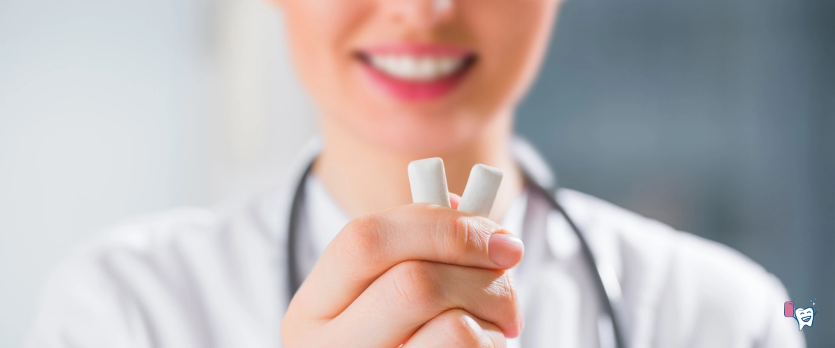 Female doctor holding two chewing gums in her right hand offering to eat and recommending dressed in a white coat over her head with a stethoscope in the background of a blurred hospital environment | For the article: Why Healthy Chewing Gum | Website: healthychewinggum.com | Source: shutterstock.com