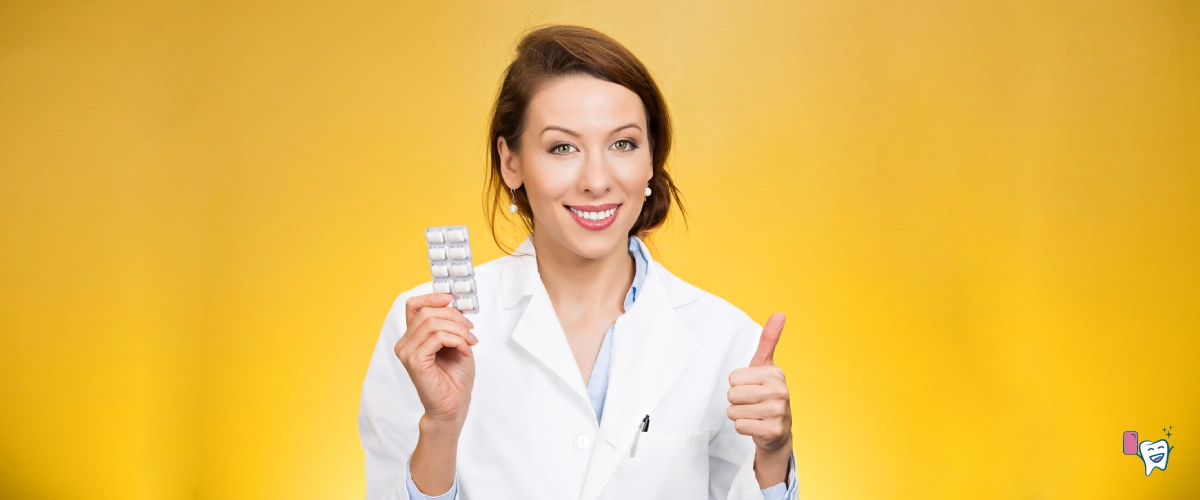 The picture a female doctor wearing a white coat with a packet of chewing gum in one hand and a thumbs-up hand gesture in the other, standing in front of an orange-brown background | For article: Chewing Gum: Regular vs Sugar-free | For website: healthychewinggum.com | Source: shutterstock