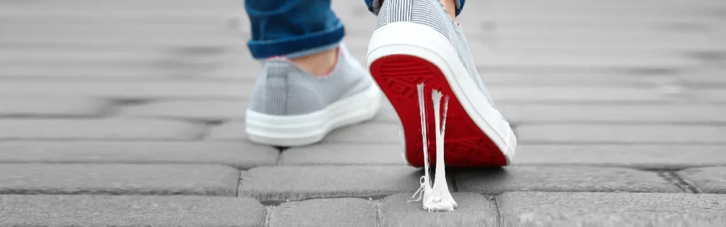 Graue Tennisschuhe, die nach links gehen und auf Kopfsteinpflaster ruhen. Zweite Bewegung mit roter Sohle und nassem, am Kaugummi klebendem Stoff, der Probleme wie 404-Fehlerseiten zeigt | Für Seite: 404 Error Seite | Für die Website: healthychewinggum.com | Quelle: Shutterstock.com