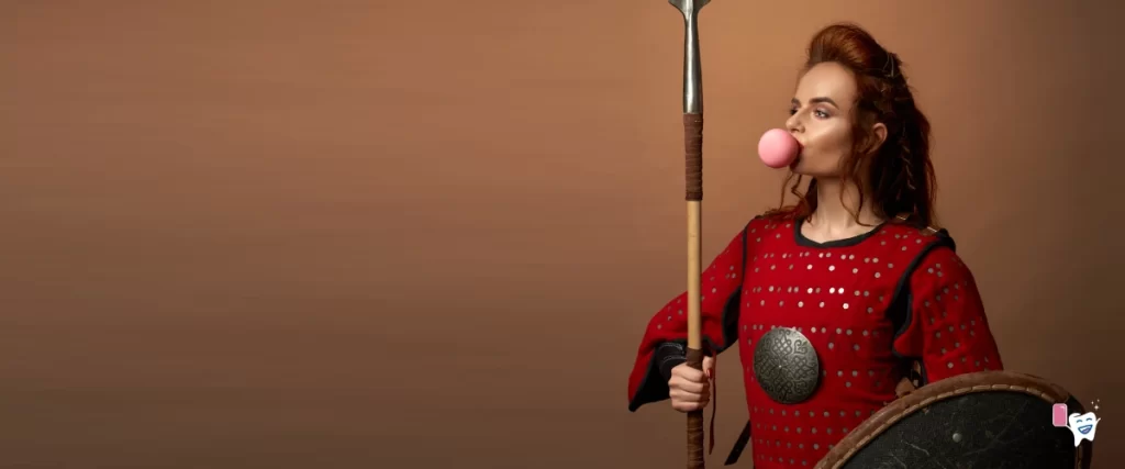 A girl warrior holding a lance and an armor blowing a chewing gum against a dark brown background | For article: Tracing the History of Chewing Gum | For website: healthychewinggum.com | Source: shutterstock