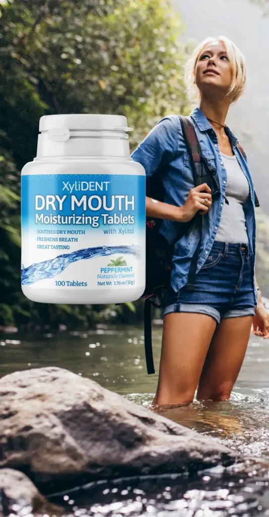 An image of a young blonde woman hiker standing in the wild nature by a river in the background of a forest and on the left a healthy moisturizing lozenge for dry mouth from the manufacturer XyliDENT | For website: HealthyChewingGum.com