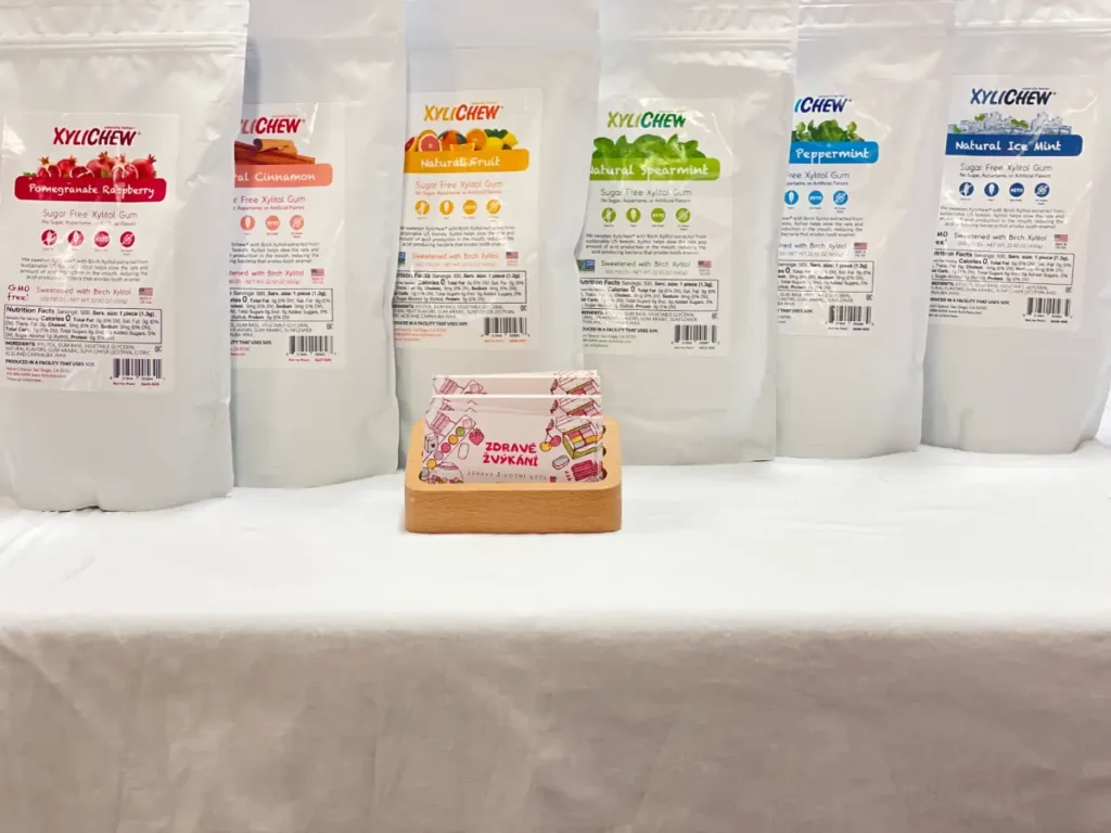 Xylichew chewing gum with cinnamon in a large bag of 500 k standing on a table with a white tablecloth in the foreground with the business card of our company Healthy Chewing - white bags with all Xylichew flavours.
