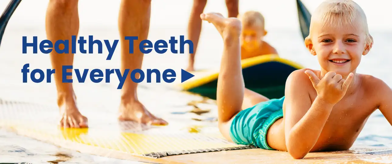 Slider banner with a smiling little boy lying in the sea on a windsurf board or paddle board with his right hand showing a gesture in the background with his brother also on a paddle board and with his parents mom and dad in the background, the ocean can be seen and the sun shining beautifully on the left - on the left side is the text in bold white letters: "Healthy Teeth for Everyone" with a small blue arrow call to action| For purposes: slider banners | For Website: HealthyChewingGum.com | Banner author: Jiří Samuel | Photo source: shutterstock.com