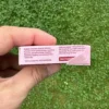 Jahodové přírodní žvýkačky Gud Gum bez plastových materiálů a bez škodlivé chemie (Britská jahoda) držené v ruce levou rukou na pozadí trávník zahrady - pohled z boku na krabičku žvýkaček - viditelný text složení a výživové údaje | Bez aspartamu, bez cukru, bez sorbitolu, bez BHT, bez BHA | Žvýkačky pro děti