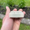 Wrapper of Lemon Chewing Gum with activated charcoal from the back held in the left hand with mint, grass and dirt in the garden in the background
