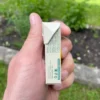 Lemon gum Gud Gum in a box from the side held in the left hand in the background with herbs, grass and a garden bed