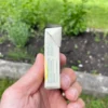 Lemon gum Gud Gum in a box from the side held in the left hand in the background with herbs, grass and a garden bed