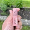 Raspberry Chewing Gum Gud Gum in a box from the side held in the left hand in the background with herbs, grass and a garden bed