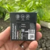 Wrapper of Charcoal Spearmint Chewing Gum with activated charcoal from the back held in the left hand with mint, grass and dirt in the garden in the background