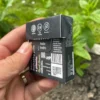 Wrapper of Charcoal Spearmint Chewing Gum with activated charcoal from the back held in the left hand with mint, grass and dirt in the garden in the background