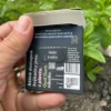 Wrapper of Charcoal Spearmint Chewing Gum from behind with activated charcoal with open wrapper, gum in palm with activated charcoal behind held in left hand with mint, grass and dirt in garden in background.