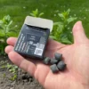 Wrapper of charcoal spearmint Chewing Gum open with chewing gum in the palm of the hand with activated charcoal in the back held in the left hand with mint, grass and dirt in the garden in the background