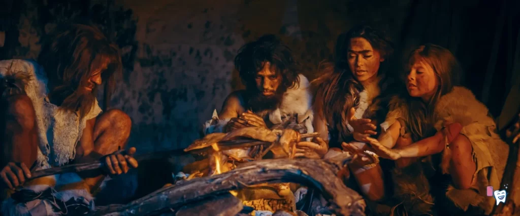 The picture shows a view into the life of ancient humans who are sitting around fire and eating | For article: History of Chewing | For website: healthychewinggum.com | Source: shutterstock