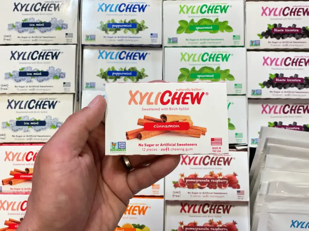 Xylichew cinnamon chewing gum in a blister holding in the left hand in the background with other blisters with other flavours