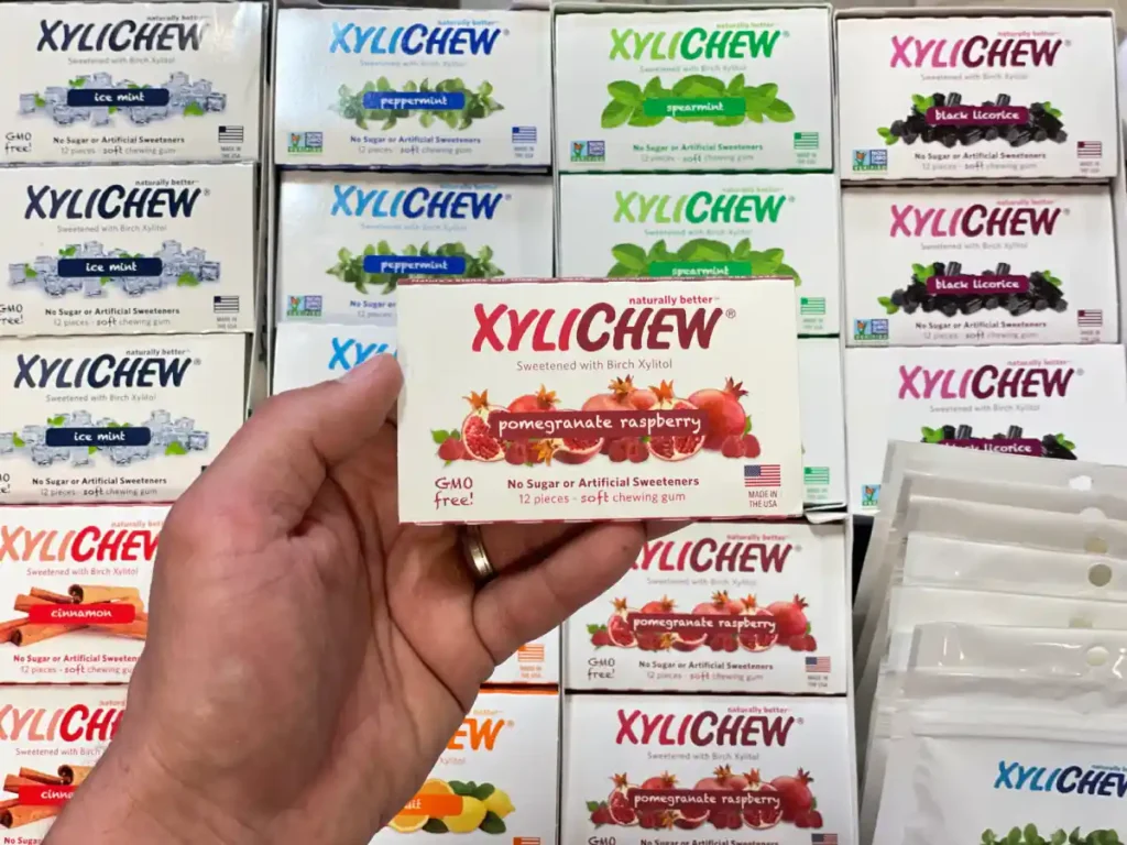 Xylichew pomegranate raspberry chewing gum in a blister holding in the left hand in the background with other blisters with other flavours